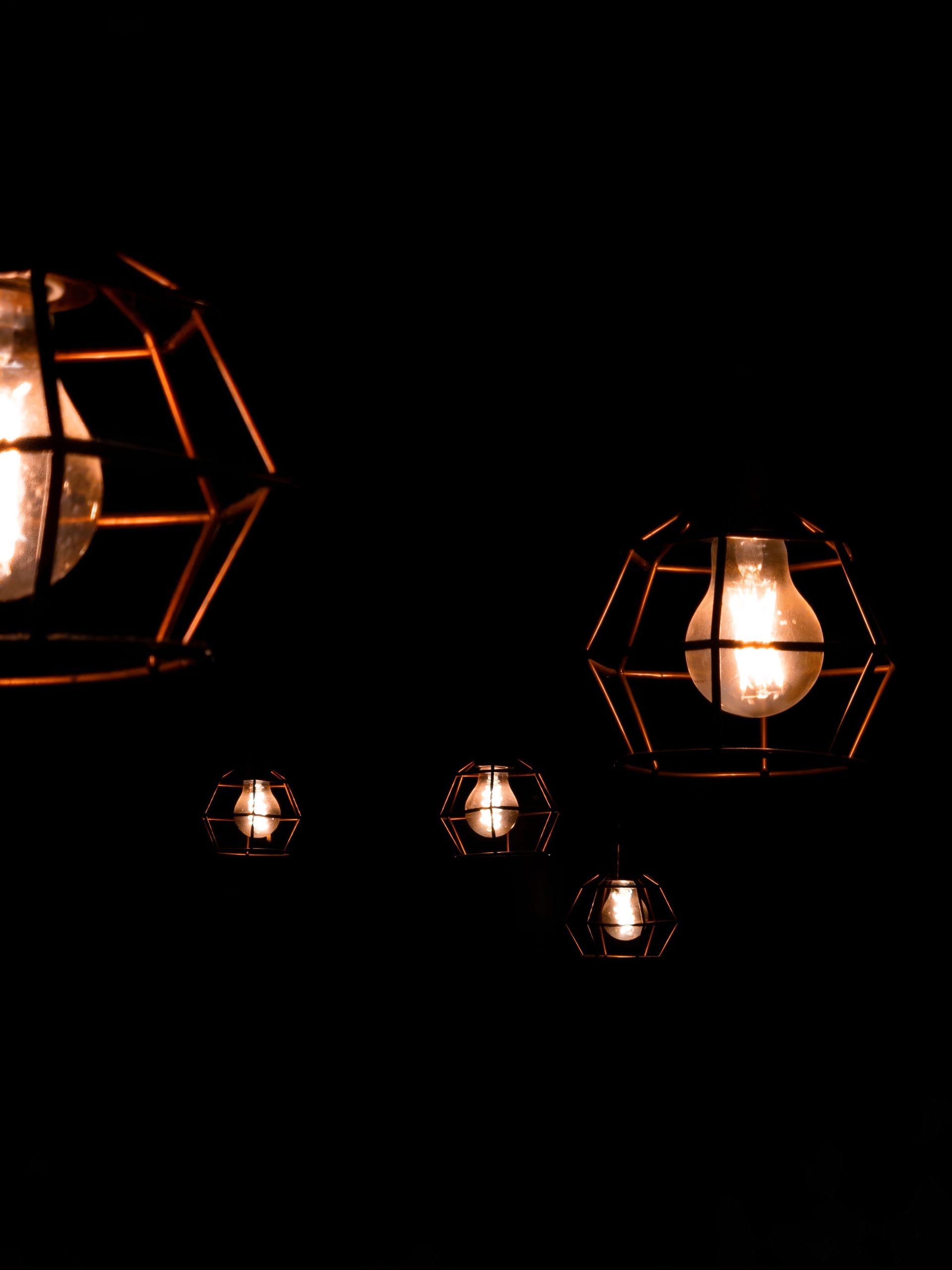 Five artistic wire cage light fixtures glowing warmly in a dark setting.